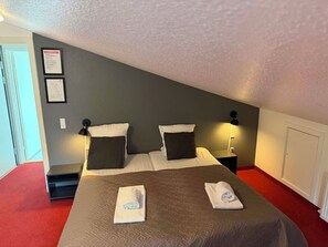A hotel room with a bed, two bedside tables, a nightstand, a wall-mounted lamp, and a door. - Hotel Kløver Es (Rodekro)