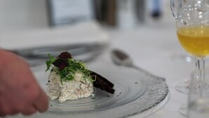 A plated dish with a garnish, a spoon, and a glass of yellow liquid on a table. - Hotel Kløver Es (Rodekro)