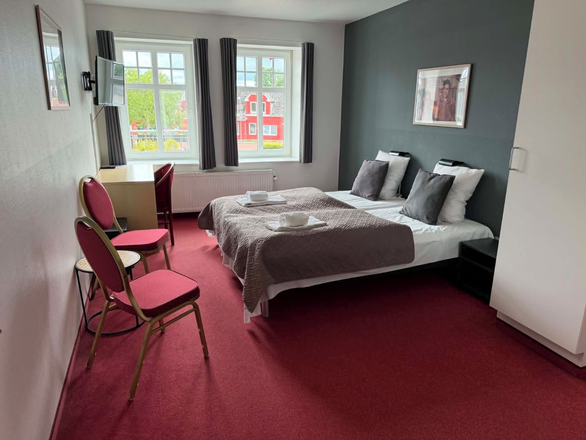 Een hotelkamer met een bed, twee stoelen, een bureau en een raam met gordijnen.