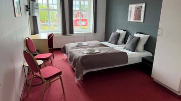 Een hotelkamer met een bed, twee stoelen, een bureau en een raam met gordijnen.