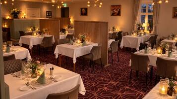 Een restaurant met meerdere tafels gedekt voor diners, elk met witte tafelkleden en kaarsen als decoratie.