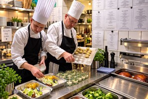 Chefs preparing food in a kitchen with stainless steel counters and menu boards on the wall. - Hotel Kløver Es (Rodekro)