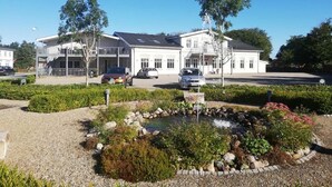A two-story building with a balcony, a small pond, and surrounding greenery. - Hotel Kløver Es (Rodekro)