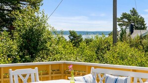 An outdoor seating area with white furniture and a table, surrounded by lush greenery and a view of a body of water. - Larkollen vacation house (Moss)