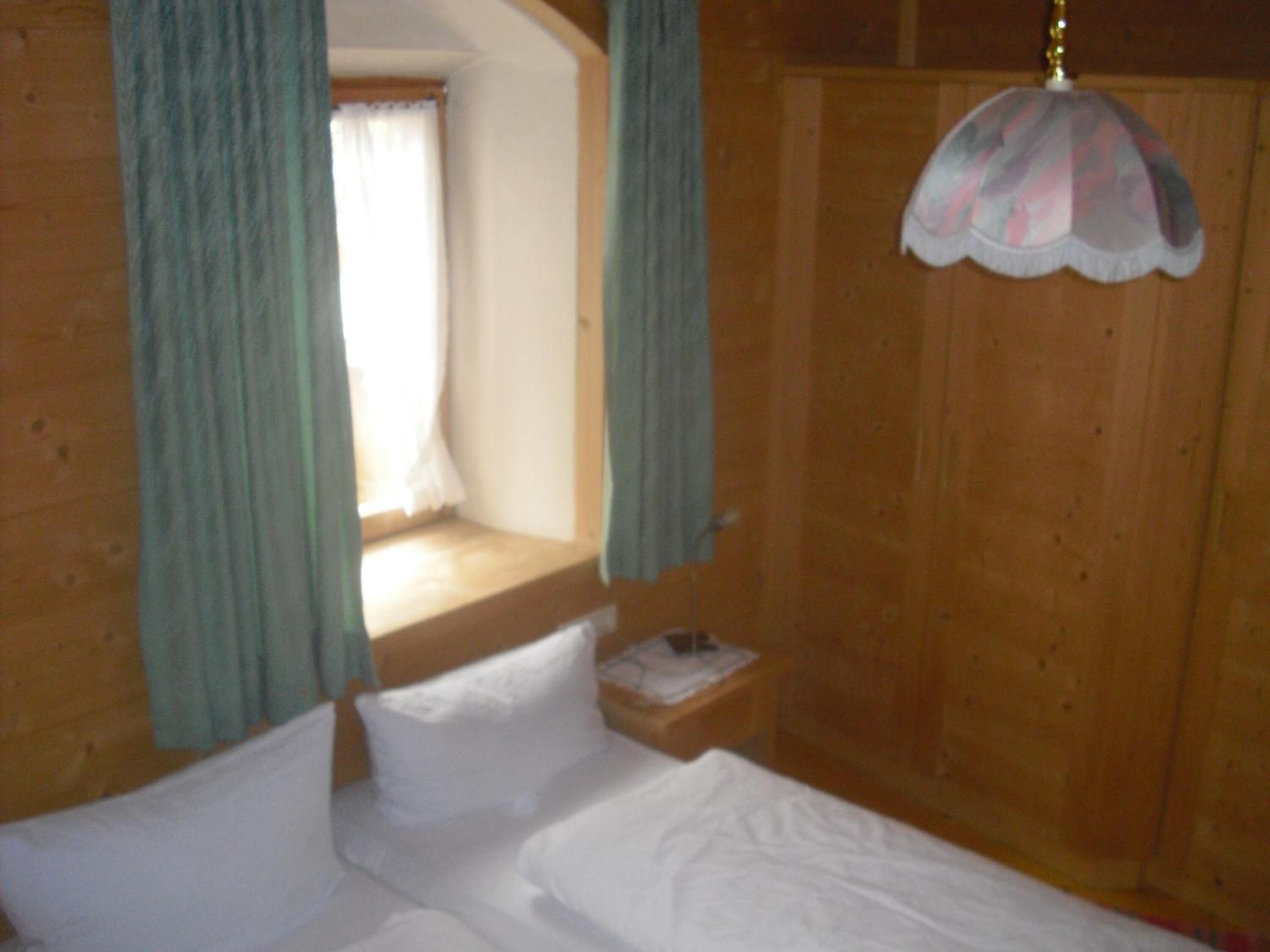 Ein Zimmer aus Holz mit einem Bett, einem Nachttisch und einem Fenster mit Vorhängen.