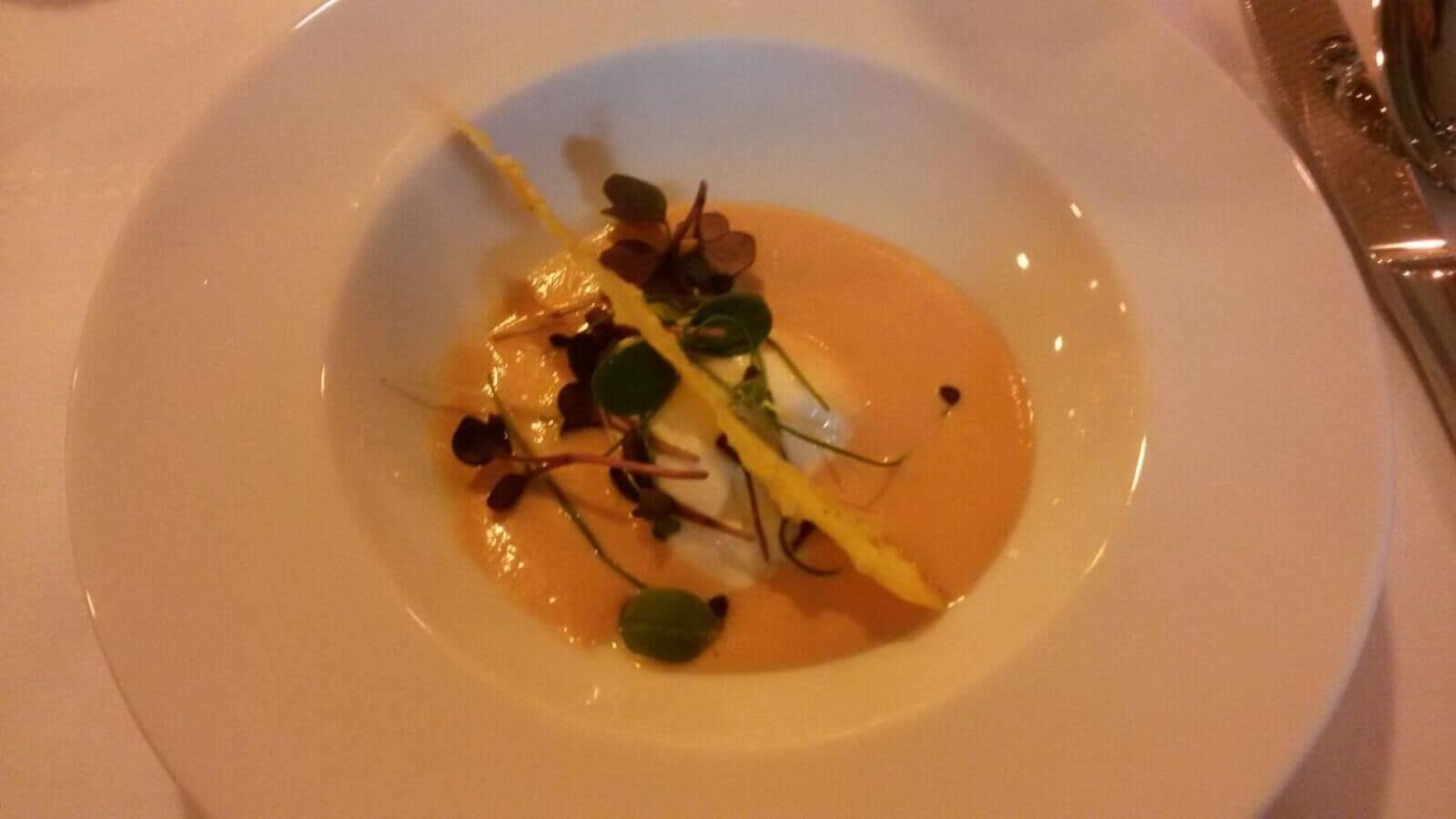 Une assiette blanche contenant un plat composé d’une sauce orange crémeuse, de feuilles vertes et d’une fine tranche de légume jaune.