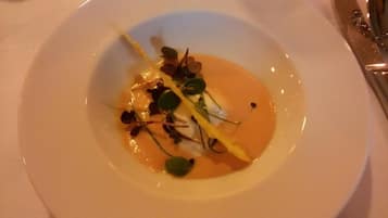 Une assiette blanche contenant un plat composé d’une sauce orange crémeuse, de feuilles vertes et d’une fine tranche de légume jaune.
