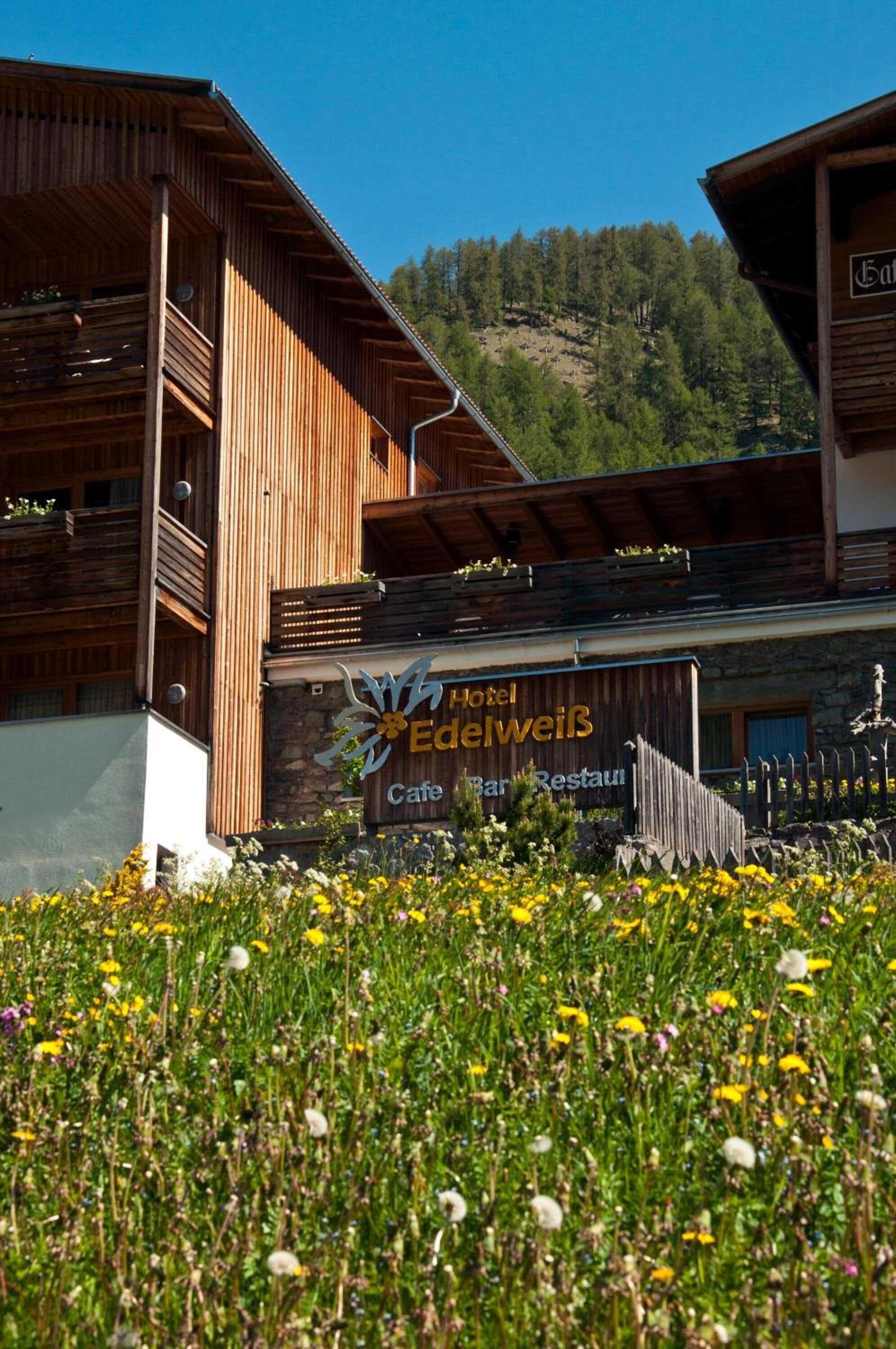 A hotel with a wooden facade and a sign reading "Hotel Edelweiß Cafe Bar Restaurant."