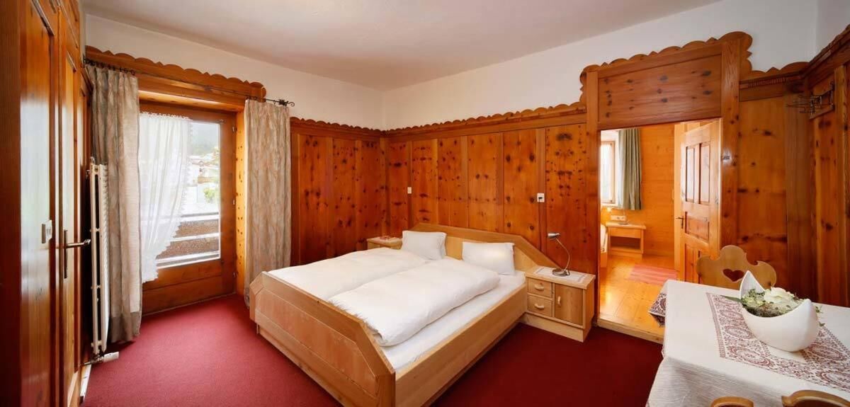 A wooden-paneled bedroom with a large bed, a bedside table, and a small table with a vase.