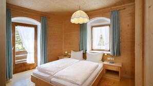 Een slaapkamer in een houten hut, met een groot bed, twee nachtkastjes, een hanglamp en gordijnen voor de ramen.