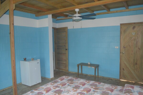 A room with a ceiling fan, a wooden door, a small table, and a refrigerator.