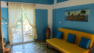 A room with a yellow sofa, blue cushions, a stone floor, a wooden bench, and a painting on the wall.