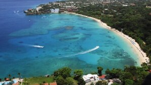 An aerial view of a coastal area with a clear blue sea, a sandy beach, and a small island with buildings. - B&B El Mirador al Mar (Sosúa)