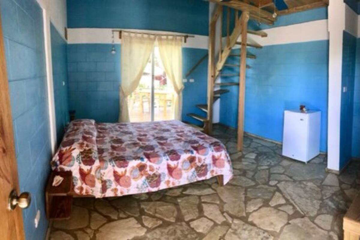 Un dormitorio con una cama, un armario pequeño blanco, una escalera de madera y una decoración en tonos azules y blancos.