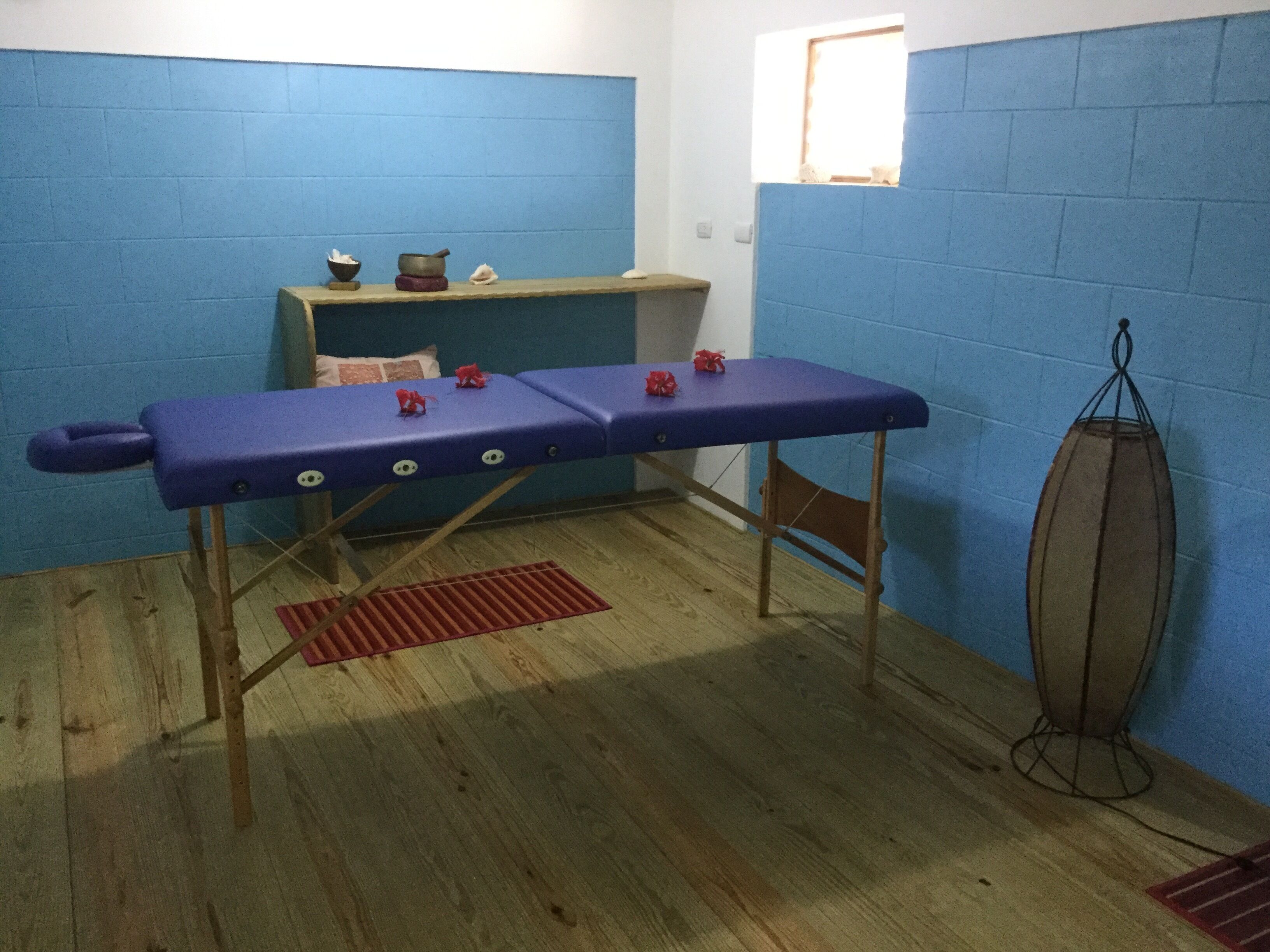 Une pièce avec une table rembourrée bleue, un petit tabouret, un tapis rouge et un ballon d’exercice suspendu au plafond.