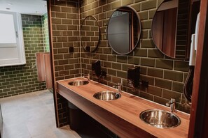 A modern bathroom with two stainless steel sinks, wooden vanity, and mirrored walls. - Durty Nelly's - Hostel (Amsterdam)
