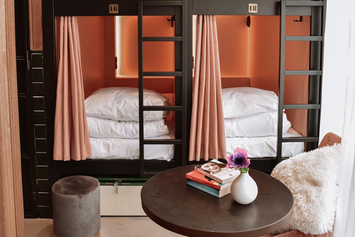 Une chambre avec un lit superposé, deux lits, une petite table ronde avec des livres et un vase, et un fauteuil rembourré.