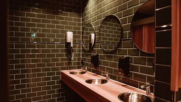 A modern bathroom with dark green tiled walls, two sinks with stainless steel basins, and round mirrors.