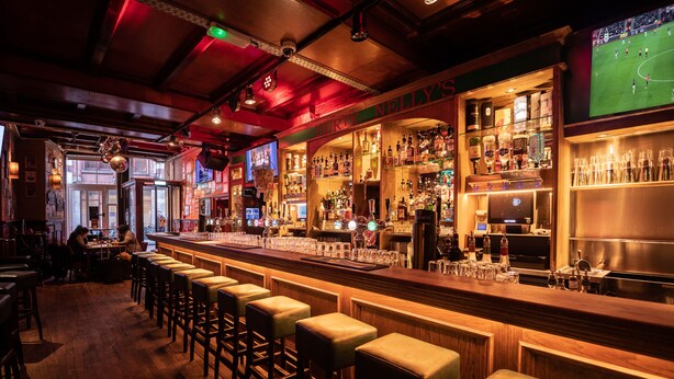 Un bar con taburetes de madera, una barra y estantes llenos de botellas.