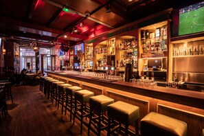 A bar with wooden stools, a bar counter, and shelves of bottles. - Durty Nelly's - Hostel (Amsterdam)