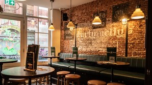 Zona de bar con paredes de ladrillo, asientos de cuero verde, iluminación colgante y un cartel de whiskey.