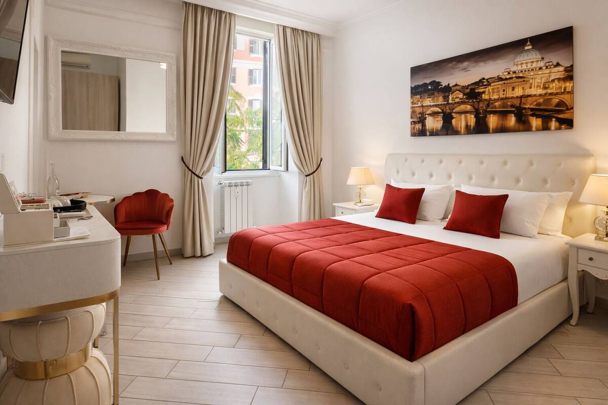 A hotel room with a large bed, a desk with a chair, a window with curtains, a radiator, and a painting on the wall.