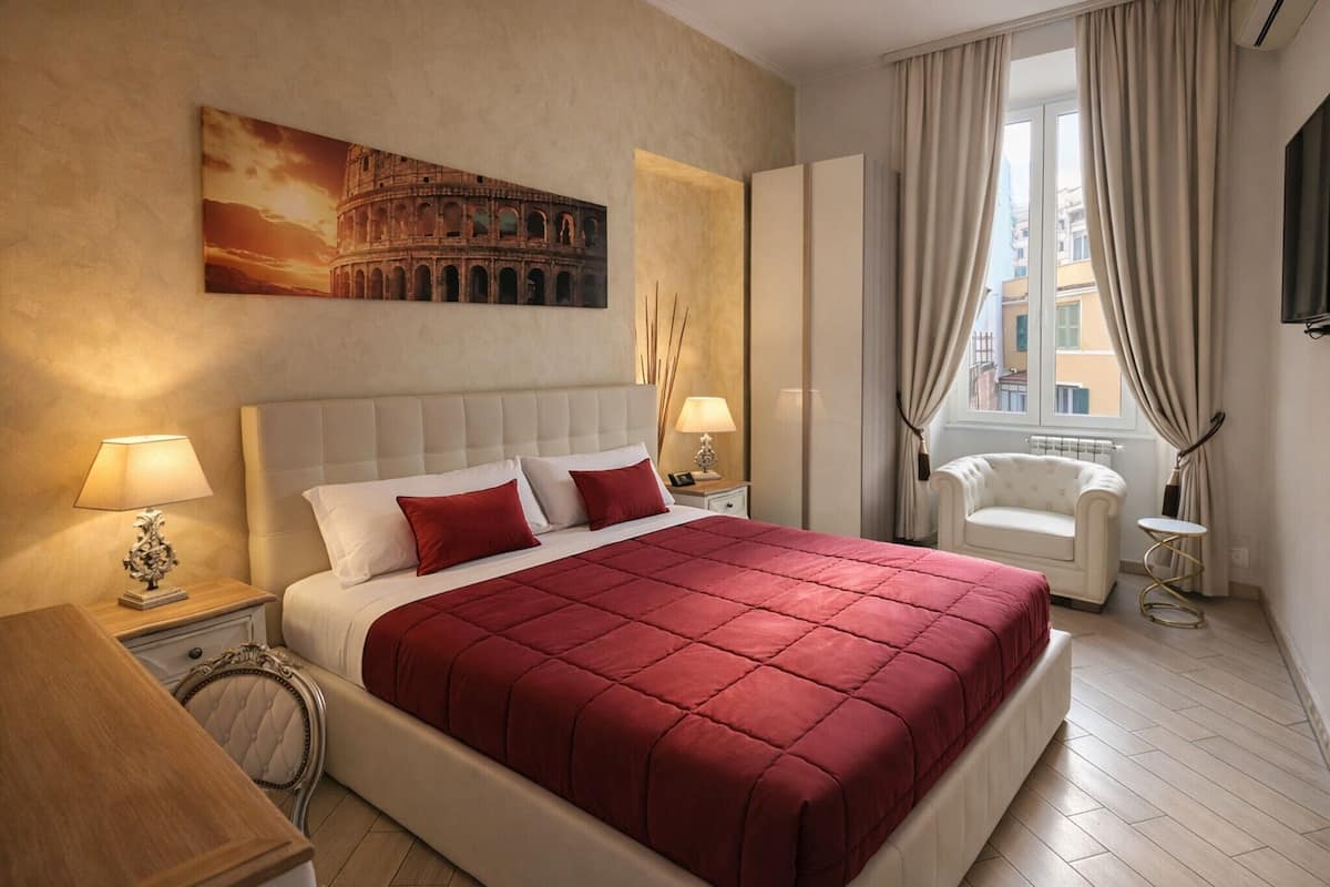 A hotel room with a large bed, a chair, a nightstand, a lamp, a painting of the Colosseum, and a window with curtains.