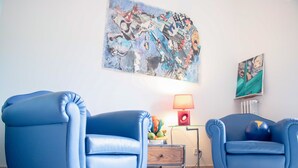 A room with two blue leather armchairs, a colorful abstract painting, a lamp, and a radiator. - Gallery (Rome)