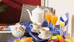 A breakfast setup with croissants, fruit, coffee, and juice on a table with a wicker chair and a wooden fence in the background. - Gallery (Rome)