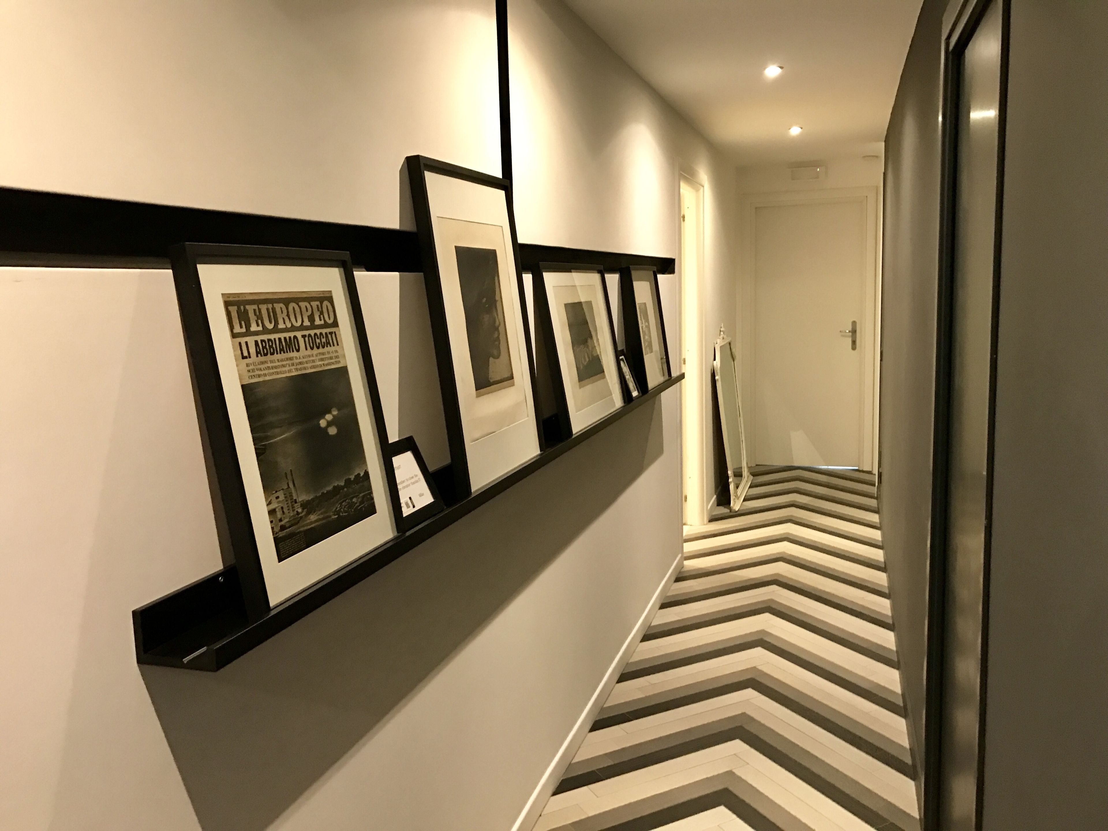 Un pasillo con un expositor de fotos enmarco negro a la izquierda y un suelo con estampado en zigzag.