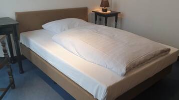 Una cama individual con cabecera de madera y una mesita de noche con lámpara.