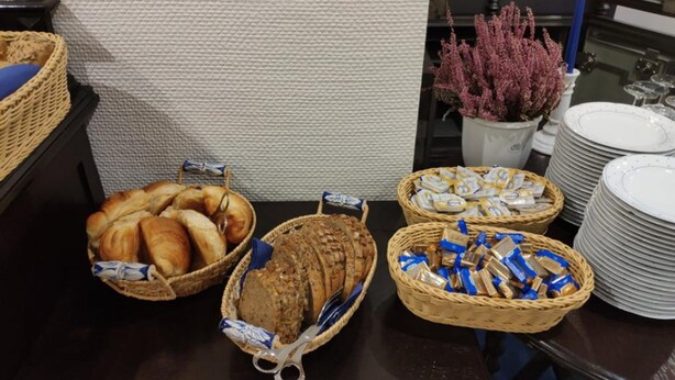 A buffet table with baskets of bread, pastries, and packaged snacks. - Hotel am Kamp (Laatzen)