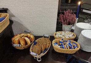 Uma mesa de buffet com cestas de pão, doces e lanches embalados.