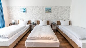 A hotel room with three single beds aligned in a row, each with a wooden headboard and white bedding. There are two bedside tables with lamps, and the walls are decorated with a textured wallpaper and two framed pictures. - Hotel am Kamp (Laatzen)