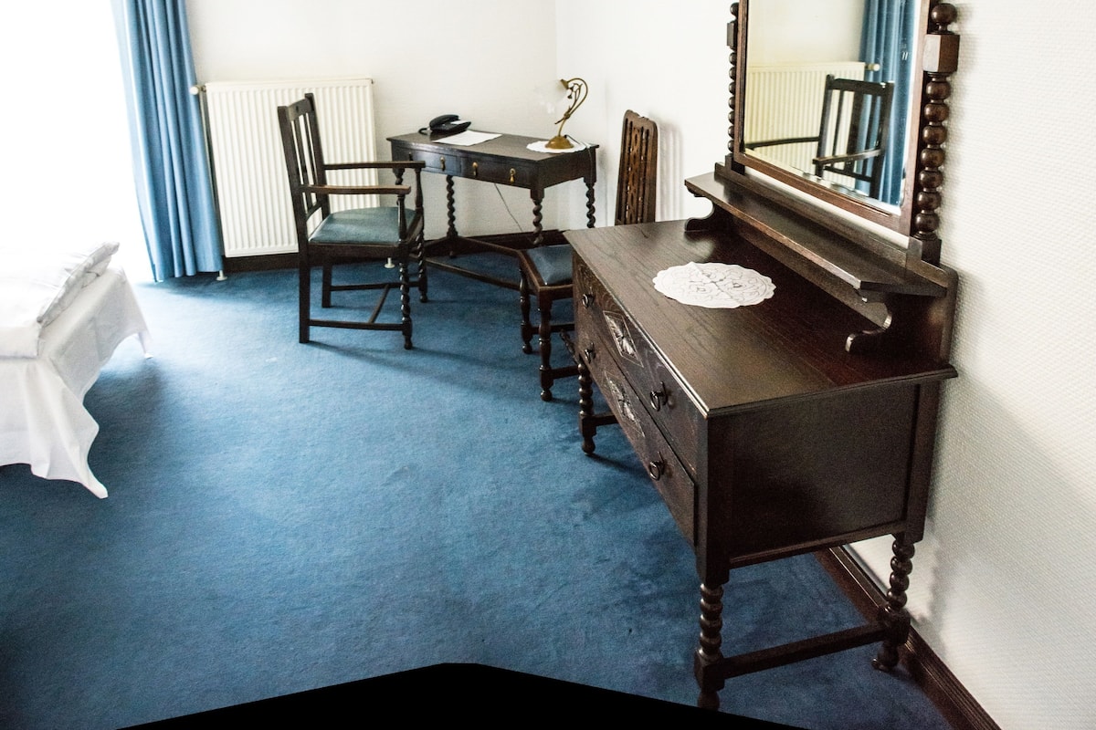 Une pièce comprenant une commode en bois, une chaise, un bureau avec un téléphone et un radiateur.
