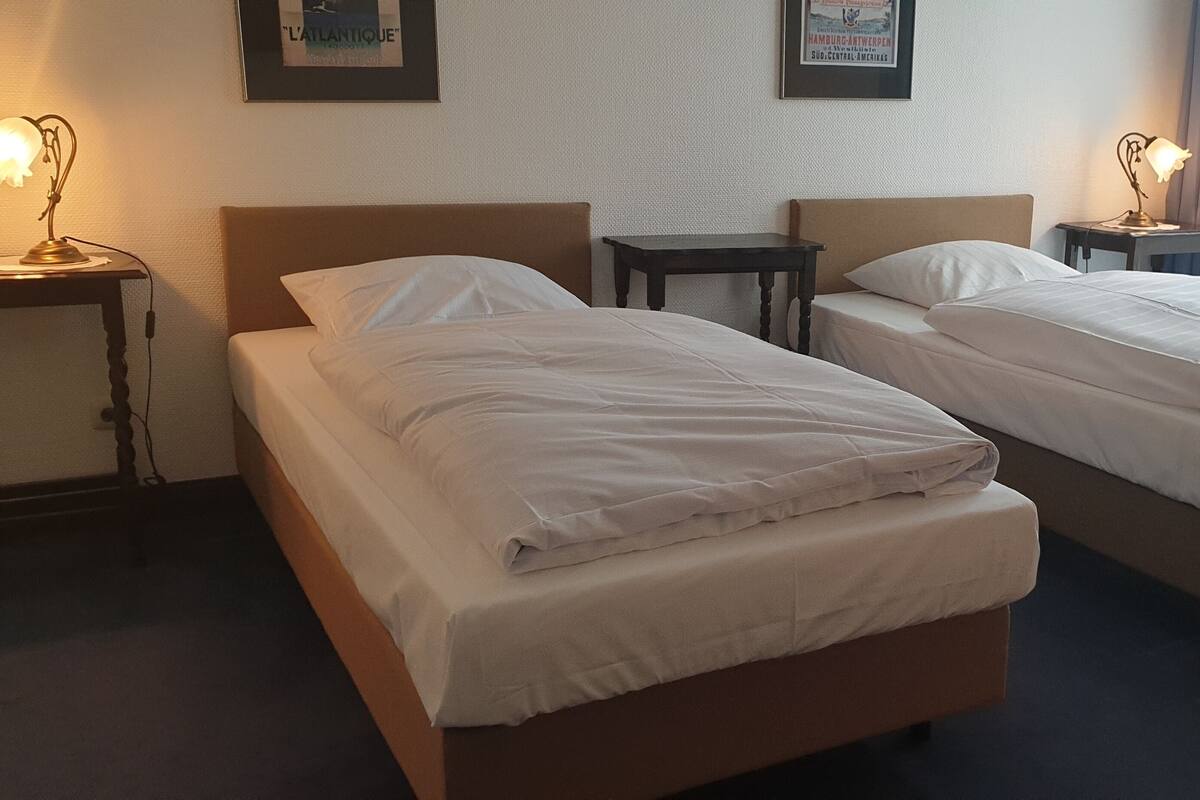 Une chambre d’hôtel avec deux lits simples, une petite table et deux lampes de chevet.