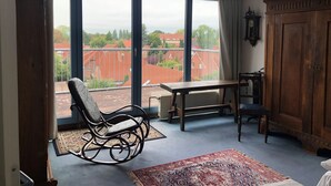 A room with a large window, a rocking chair, a wooden table, and a cabinet. - Hotel am Kamp (Laatzen)