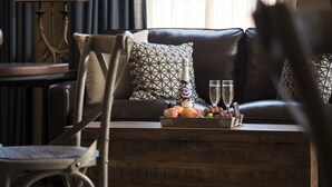 Ein Wohnzimmer mit Ledersofa, gemusterten Kissen, einem Couchtisch mit Obst und Gläsern sowie einem Sessel.