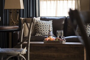Una sala de estar con un sofá de cuero, almohadas estampadas, una mesa de centro de madera con frutas y vasos, y un sillón.