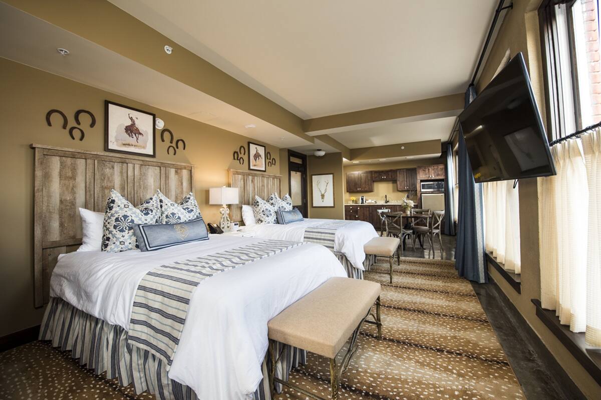 A hotel room with two beds, a bench, a desk, and a TV.