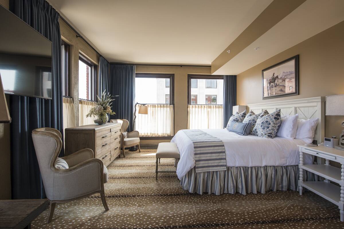 A hotel room with a large bed, a desk, a chair, a dresser, and a window with curtains.