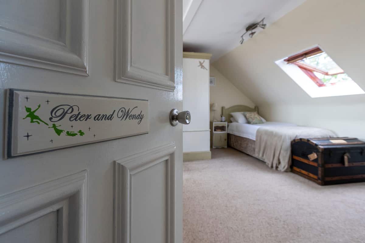 A bedroom with a bed, a nightstand, a suitcase, and a window with a view of the outdoors.