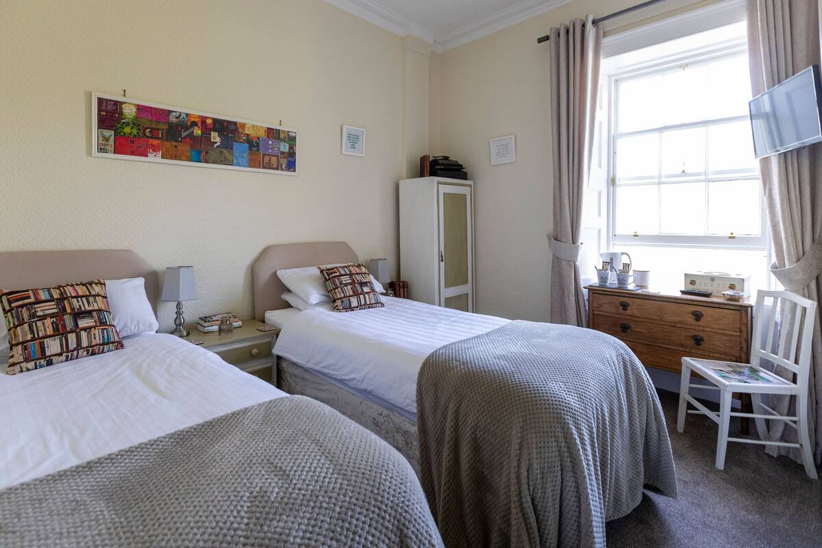 A hotel room with two beds, a wardrobe, a desk with a chair, and a window with curtains.