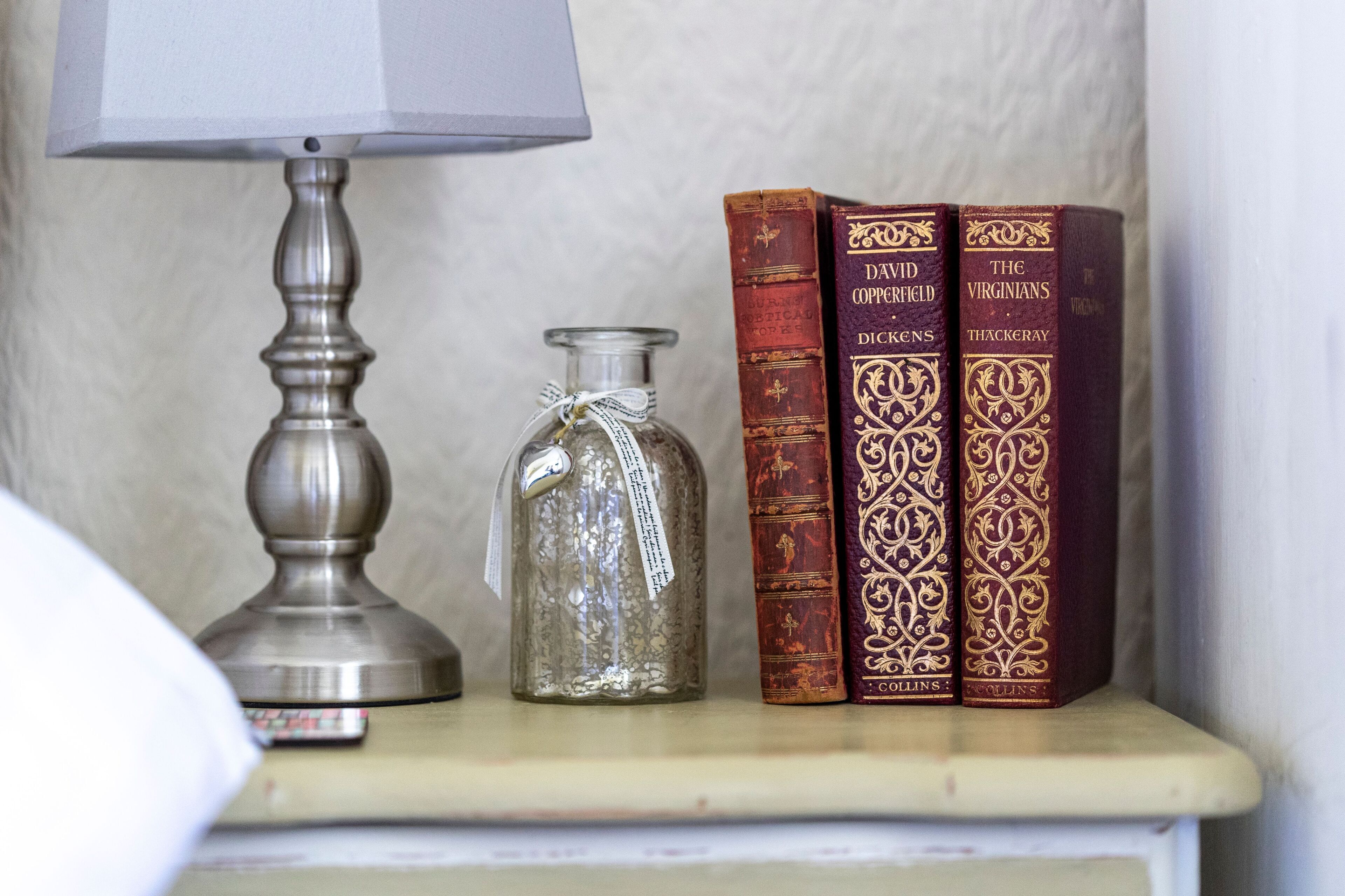 A shelf with a lamp, a glass bottle, and three books.