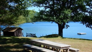 Un área de picnic junto al lago con una mesa y bancos de madera, un cobertizo pequeño y un muelle con un bote.