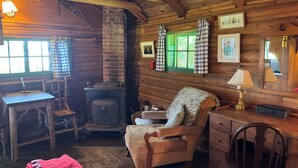 Interior acogedor de una cabaña con detalles de madera, una chimenea, una mesa con lámpara y una silla.