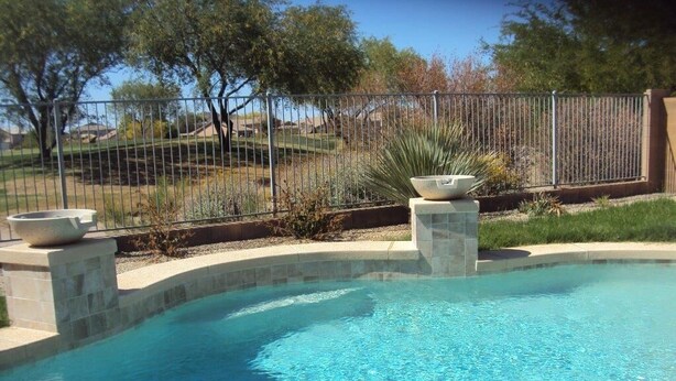 A swimming pool with a clear blue water, surrounded by a stone border and a metal fence. - *SUMMER SPECIALS** Scenic Golf Course 3 Bed Home w/ Private Pool and Hot Tub (Queen Creek)