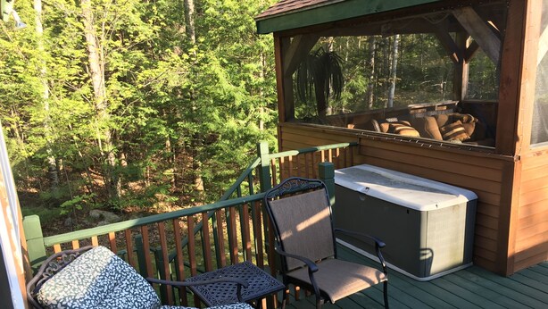 Une terrasse en bois avec des meubles d’extérieur, un jacuzzi et une vue sur une forêt.