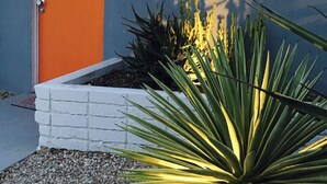 Ein Gebäude mit einer orangen Tür, einem weißen Ziegelkübel und einer großen Yucca-Pflanze.