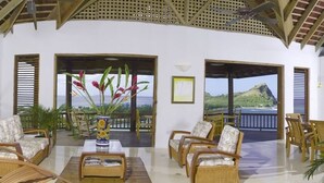 A spacious room with wicker furniture, large windows, and a view of the ocean. - Zandoli Villa
Simply Awesome Views (Cap Estate)